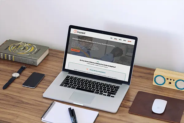 A laptop open on a wooden desk showing the desktop homepage of a Richmond-based electrician website, Connect Electric.